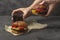 Male holding freshly prepared grilled beef burger above a dark background. Man serves burger to the table. American snack