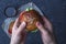 Male holding freshly prepared grilled beef burger above a dark background. Man serves burger to the table. American snack