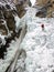 Male ice climber in a red jacket rappelling off a dangerous nd collapsing ice fall in deep winter