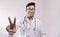 Male indian doctor in white coat and stethoscope showing victory sign in confidence
