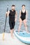 Male instructor and young woman standing with paddleboard on the beach