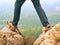 Male legs in dark hiking trousers and leather trekking shoes on peak of rock above misty valley. Outline of hill
