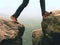 Male legs in dark hiking trousers and leather trekking shoes on peak of rock above misty valley. Outline of hill