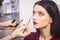 Male make-up artist doing brunette girl make-up in beauty salon, close-up