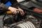 A male mechanic with a can spray gasoline into the intake manifold to start the car during engine breakdown of the ignition and