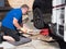 A male mechanic kneels down on a kneeling mat using a trolley jack ready to lift a motorhome front wheel. RV