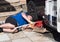 A male mechanic lying down as he places a red trolley jack under front of a motorhome recreational vehicle