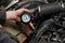 A male mechanic measures the compression in the cylinder of a car engine using a barometer with a scale and an arrow during