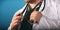 Male medicine therapeutist doctor hands holding stethoscope on his chest in the hand closeup. Physician is waiting for patient