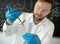 Male microbiologist holding a young plant with a syringe in it while working in a food lab, growing gmo plants in a lab