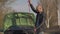 A male motorist holds an electric cable while standing by a car with the hood open.