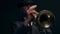 Male musical artist playing trumpet in rays of spotlight on dark background, front view. Man plays jazz trumpet in dark