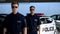 Male officers in sunglasses standing against squad car, ready for patrolling