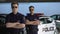 Male officers in sunglasses standing with hands crossed against police car