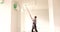 Male painter builder paints ceiling with roller in room
