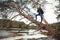 Male photographer photographing a beautiful taiga river, standing on a fallen pine tree