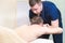 A male physiotherapist does a power stretching for a male patient to a young bearded hipster in a medical massage room