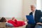 A male psychotherapist writes on a clipboard during a patient consultation. An emotional woman in a red dress lies on a