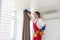 A male repairman installs a curtain rod and hangs curtains in the house. services to help with household chores and