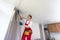 A male repairman installs a curtain rod and hangs curtains in the house. services to help with household chores and