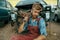 Male repairman sitting on the ground, car junkyard