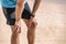 Male runner resting taking a break tired with knee pain after beach jog wearing smartwatch wearable technology for
