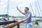 Male sailor waving up on pier and smiling. Yachtsman gives the command by hand to moor in dock. Man welcomes newcoming boat