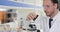 Male Scientist Working With Microscope Looking At Test Tube In Laboratory Wearing White Coat And Protective Glasses