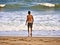 Male silhouette goes in the sea water on a sand beach. Young adult boy on the beach - beautiful background with copy space
