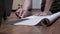 Male, Sitting on Floor, Cuts off a Strip of Wallpaper for Pasting with a Knife