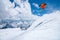 A male skier in an orange suit flies in the air after jumping from a snow sweep high in the Caucasian mountains on a