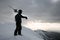 male skier in ski suit with skis on his shoulders stands on snow-covered mountain peak