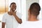 Male Skincare. Handsome Black Guy Looking In Mirror In Bathroom, Touching Beard