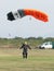 Male skydiver making safe landing landing on grass with open bright colourful parachute.