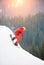 Male snowboarder freerider in a red suit riding from the top of the snowy hill with snowboard