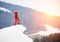 Male snowboarder standing on the top of the snowy hill with snowboard, enjoying sunset