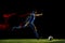 Male soccer player kicking ball on dark background in mixed light