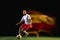 Male soccer player kicking ball on dark background in mixed light