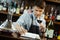 Male sommelier tasting red wine and making notes at bar counter