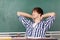 Male Student Relaxing At Desk Against Chalkboard