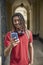 Male Student Wearing Wireless Headphones Checking Messages Or Social Media On Mobile Phone Outside University Building In Oxford