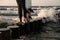 Male surfer legs in wetsuit standing on wooden stump near surfboard