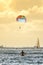 Male surfer sitting on his board looking at a rainbow parasailing parachute in Hawaii