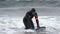 Male surfer sportsperson in black wetsuit cruising along breaking wave in Pacific Ocean