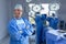 Male surgeon standing with arm crossed in operation room while surgeons getting ready for operation