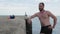 Male swimmer with a beard is standing on a concrete pier after swimming in the sea in the background a lighthouse. 4k. 4k video