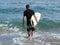 Male in swimsuit going in water with surfboard.