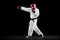 Male taekwondo fighter in white dobok, helmet and gloves training isolated over dark background. Concept of sport