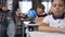 Male teacher of elementary school walking between desks puts computers tablet on desk pupils for learning