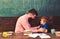 Male teacher explaining something to the boy. Side view bearded man in glasses and blond child in front of green board